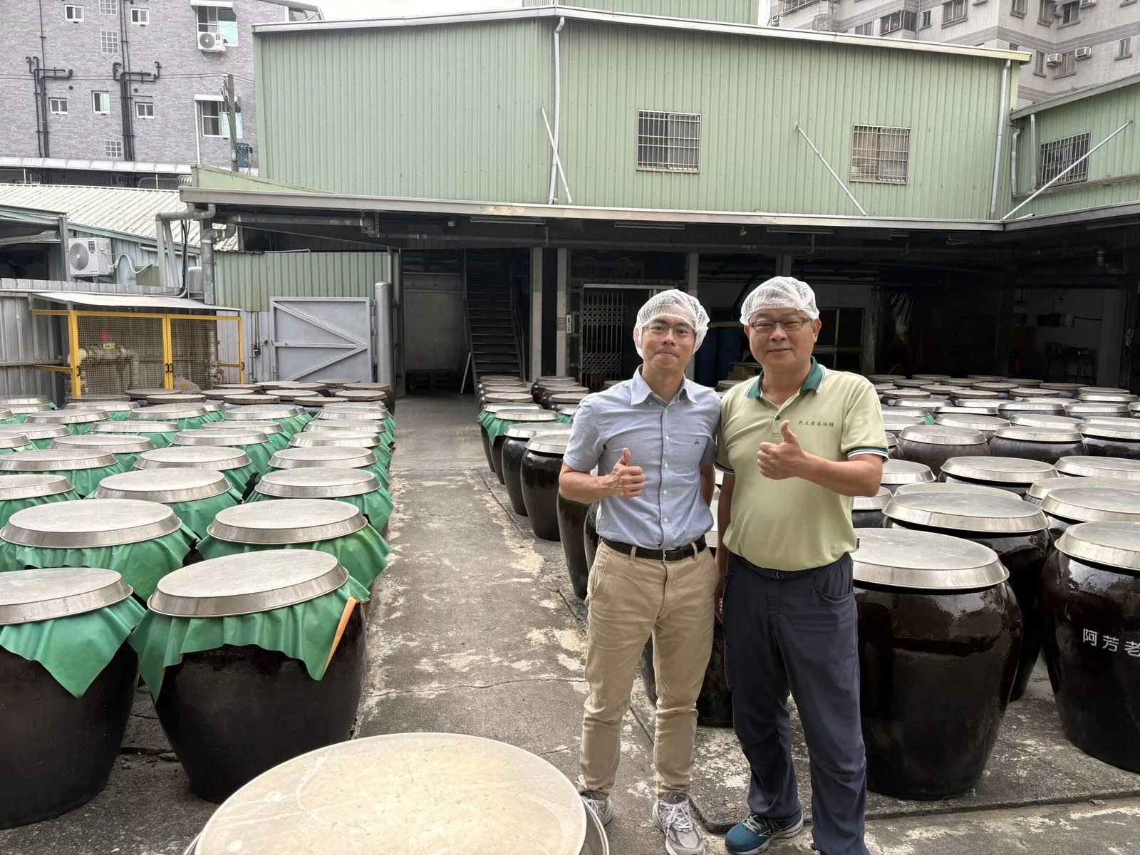 思思醫師與民生食品工廠第二代經營者鄭惠民，在曬缸場的陶缸之間合影